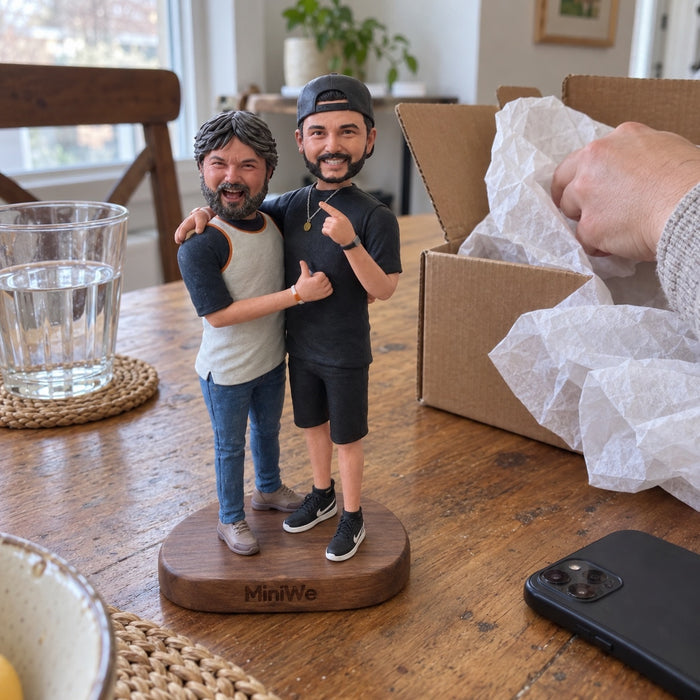 A two-person figurine beside an open shipping box on a dining table.